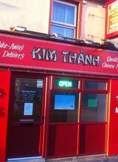 Image of a red storefront for a Chinese take-away and delivery restaurant called "Kim Thành." The sign above the door displays the restaurant's name and "Quality Chinese Food" in capital letters. A bright neon "OPEN" sign is visible in the window.